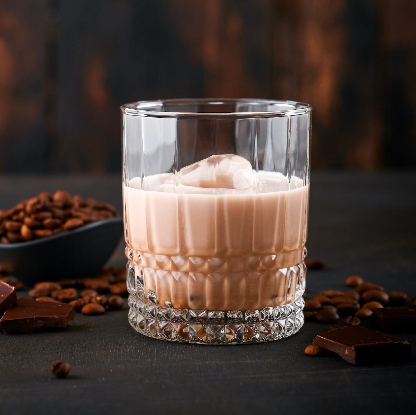 Glass of Irish cream baileys liqueur with roasted coffee beans, cinnamon and chocolate on dark wood
